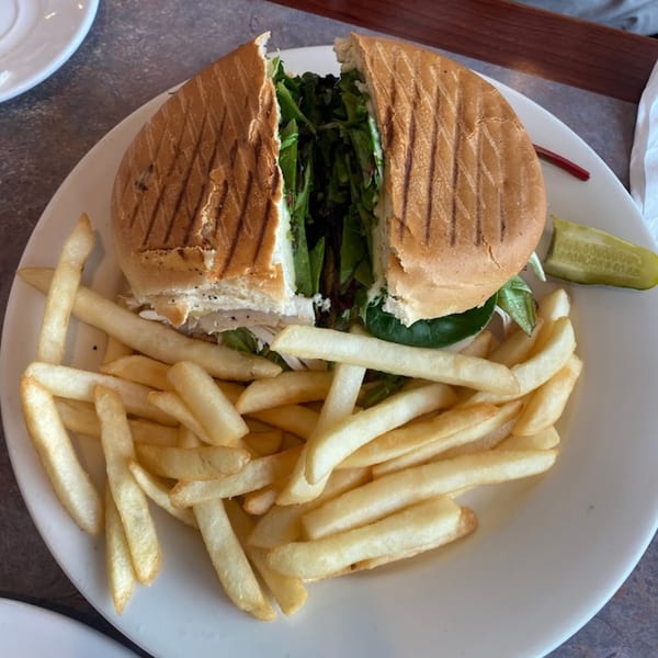A Lighthouse Diner panini sandwich, cut in half, with fries and a pickle spear on a white plate.