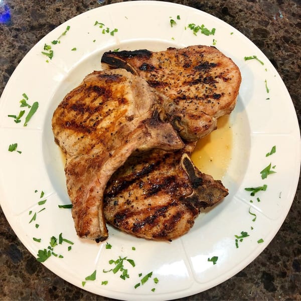 Three grilled pork chops with grill marks and parsley garnish on a white plate at Lighthouse Diner.