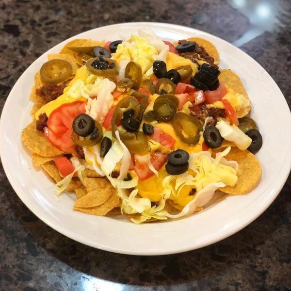 A plate of Lighthouse Diner nachos with cheese, jalapeños, olives, tomatoes, and shredded lettuce.