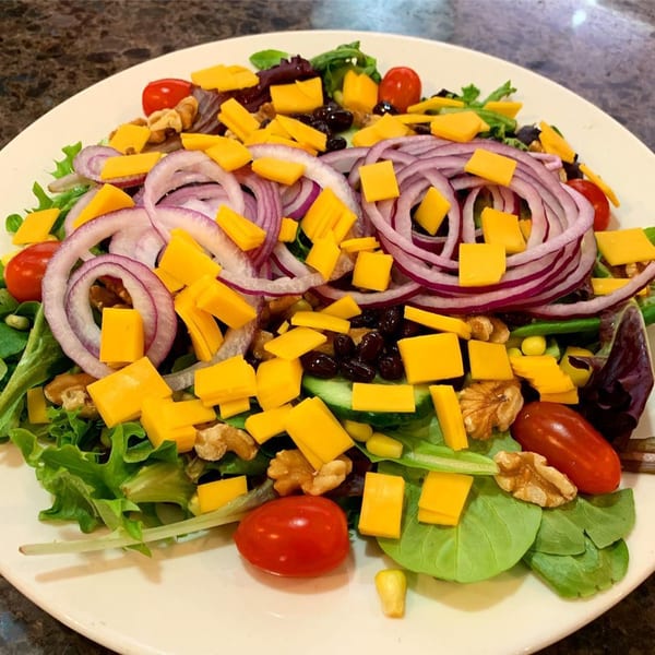 A fresh Lighthouse Diner salad with mixed greens, red onion, cherry tomatoes, cheese, walnuts, and beans.