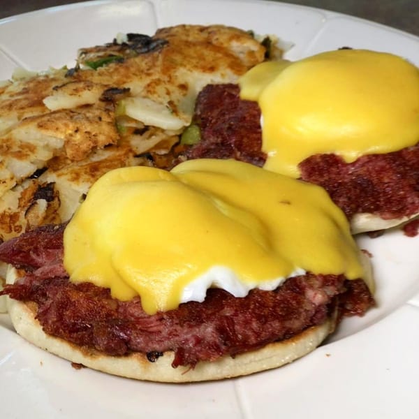 Corned beef hash Benedict with hollandaise sauce and a side of crispy hash browns.